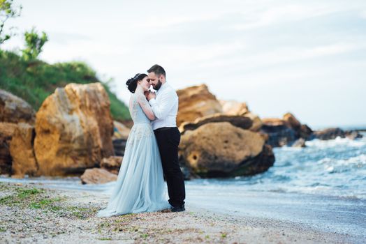 same couple with a bride in a blue dress walk along the ocean shore