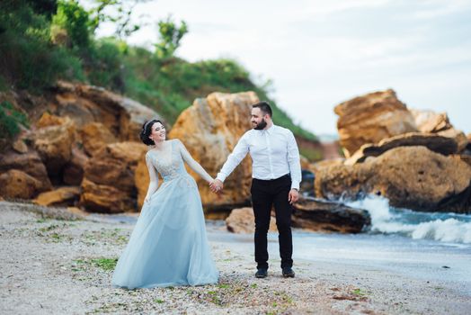 same couple with a bride in a blue dress walk along the ocean shore