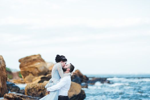 same couple with a bride in a blue dress walk along the ocean shore