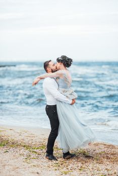 same couple with a bride in a blue dress walk along the ocean shore