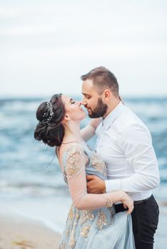 same couple with a bride in a blue dress walk along the ocean shore