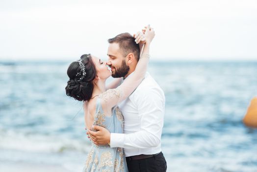 same couple with a bride in a blue dress walk along the ocean shore