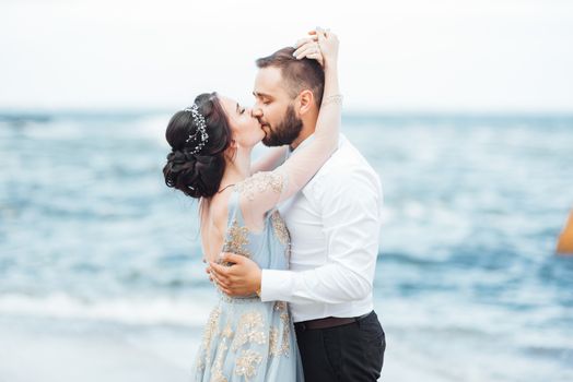 same couple with a bride in a blue dress walk along the ocean shore