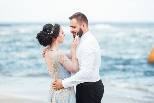 same couple with a bride in a blue dress walk along the ocean shore