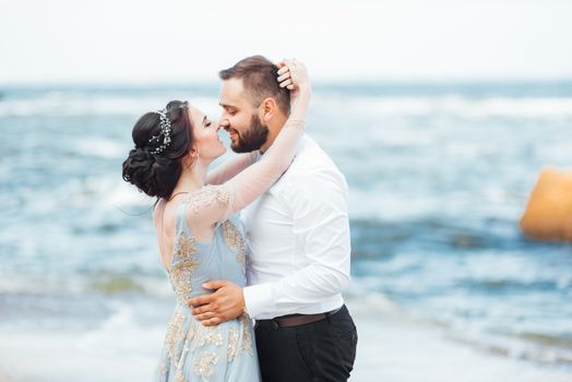 same couple with a bride in a blue dress walk along the ocean shore