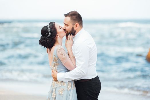 same couple with a bride in a blue dress walk along the ocean shore