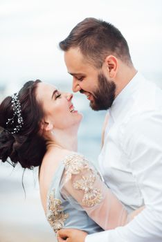 same couple with a bride in a blue dress walk along the ocean shore