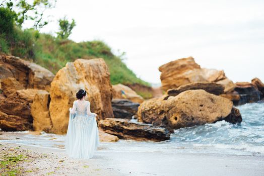 bride in a blue light dress walking along the ocean