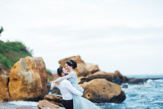 same couple with a bride in a blue dress walk along the ocean shore