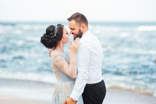 same couple with a bride in a blue dress walk along the ocean shore