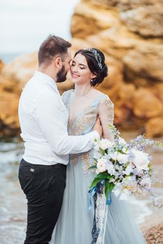 same couple with a bride in a blue dress walk along the ocean shore