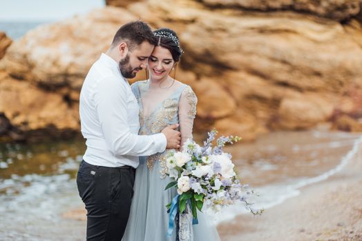 same couple with a bride in a blue dress walk along the ocean shore