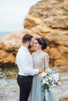 same couple with a bride in a blue dress walk along the ocean shore