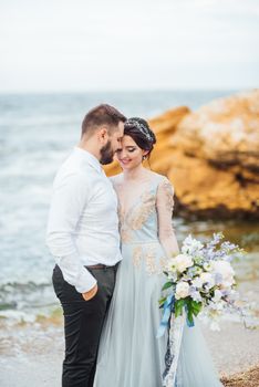 same couple with a bride in a blue dress walk along the ocean shore