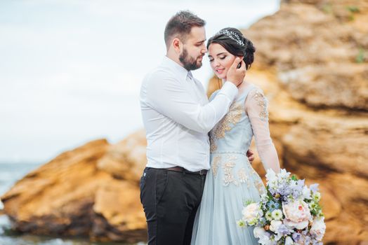 same couple with a bride in a blue dress walk along the ocean shore