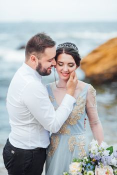 same couple with a bride in a blue dress walk along the ocean shore