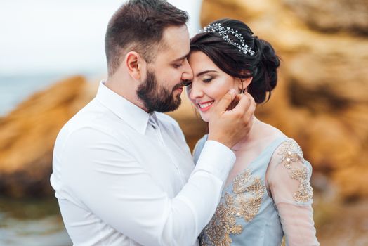 same couple with a bride in a blue dress walk along the ocean shore