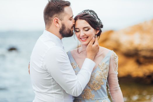 same couple with a bride in a blue dress walk along the ocean shore