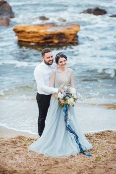 same couple with a bride in a blue dress walk along the ocean shore