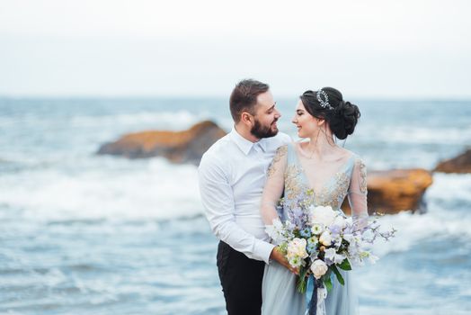 same couple with a bride in a blue dress walk along the ocean shore