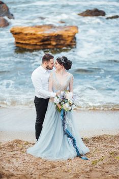 same couple with a bride in a blue dress walk along the ocean shore