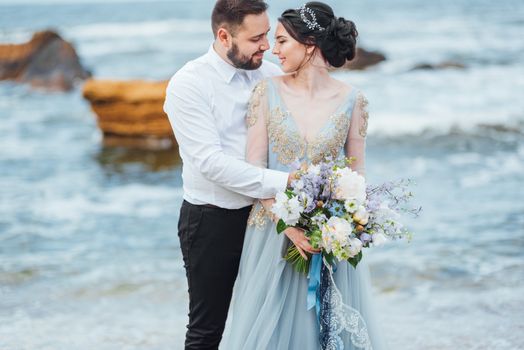 same couple with a bride in a blue dress walk along the ocean shore