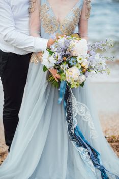 same couple with a bride in a blue dress walk along the ocean shore