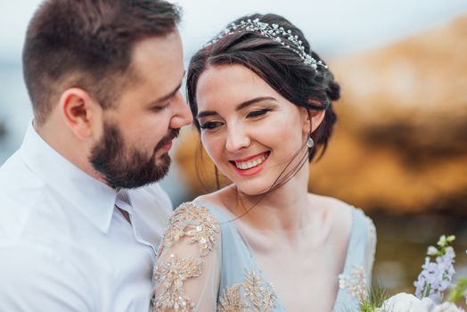 same couple with a bride in a blue dress walk along the ocean shore