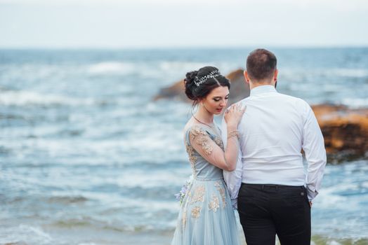 same couple with a bride in a blue dress walk along the ocean shore