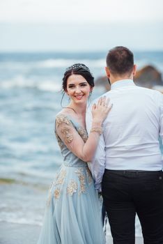 same couple with a bride in a blue dress walk along the ocean shore