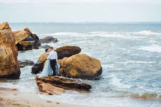 same couple with a bride in a blue dress walk along the ocean shore