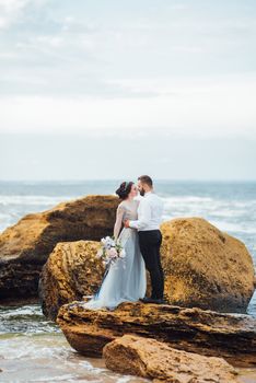 same couple with a bride in a blue dress walk along the ocean shore