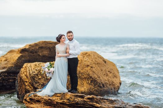 same couple with a bride in a blue dress walk along the ocean shore