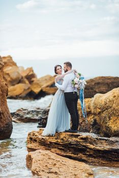 same couple with a bride in a blue dress walk along the ocean shore