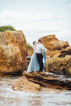 same couple with a bride in a blue dress walk along the ocean shore