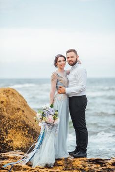 same couple with a bride in a blue dress walk along the ocean shore