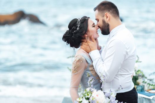 same couple with a bride in a blue dress walk along the ocean shore