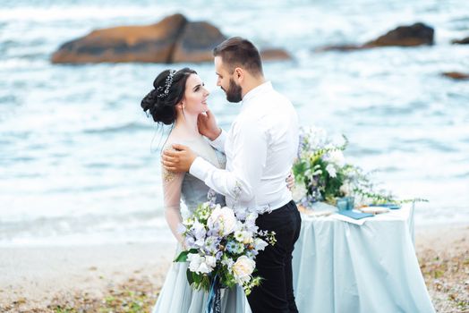 same couple with a bride in a blue dress walk along the ocean shore