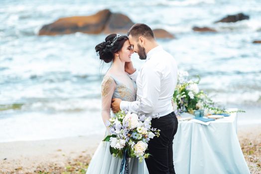 same couple with a bride in a blue dress walk along the ocean shore