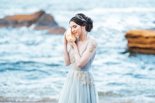 bride with a big shell on the beach in a blue wedding dress