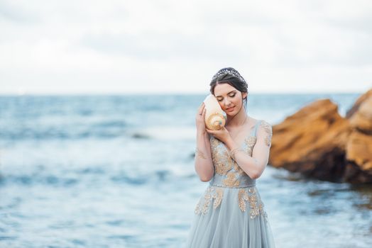 bride with a big shell on the beach in a blue wedding dress