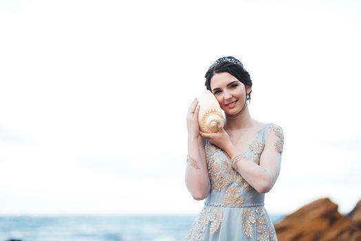 bride with a big shell on the beach in a blue wedding dress