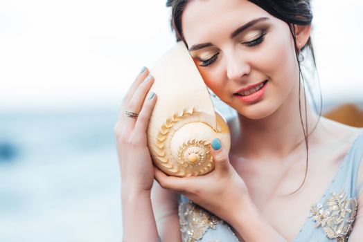 bride with a big shell on the beach in a blue wedding dress