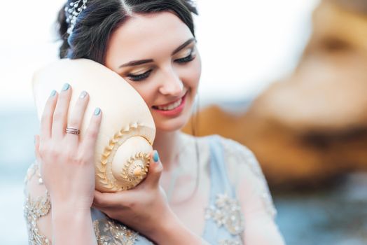 bride with a big shell on the beach in a blue wedding dress