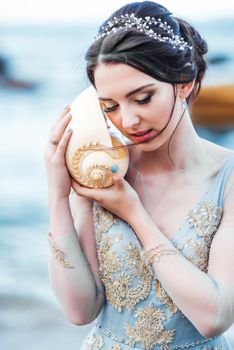 bride with a big shell on the beach in a blue wedding dress