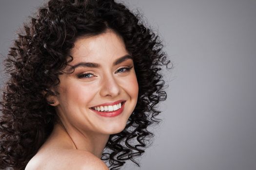 Fashion studio portrait of beautiful smiling woman with curls hairstyle. Fashion and beauty