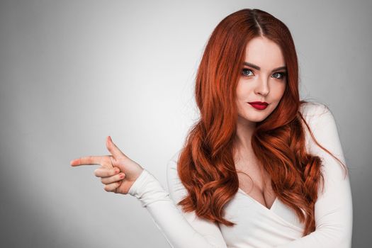 Portrait of young woman with long beautiful ginger hair pointing aside