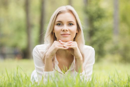 Blonde pretty girl laying on the grass in spring park and smiling