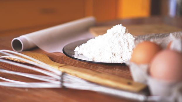 Ingredients for baking homemade bread. Eggs, flour. Wooden background, side view. Soft focus and light