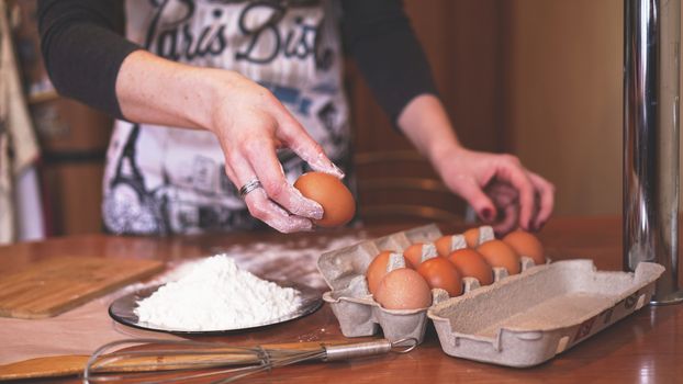 The hands of a female chef picking an egg for making dough while making bread with a pile of wheat nearby